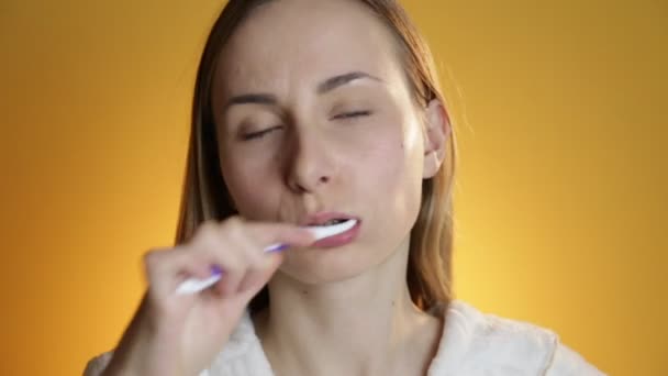 Woman brushing her teeth and smiling against yellow background — Stock Video