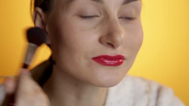 Beautiful happy young lady putting makeup on a yellow background — Stock Video