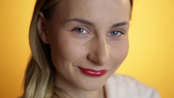 Передний портрет красивой улыбающейся женщины, смотрящей в камеру на желтом фоне — стоковое видео