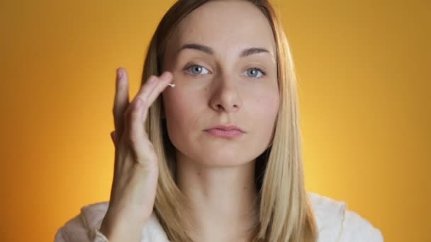 Hermosa modelo de poner crema facial sobre fondo amarillo — Vídeos de Stock