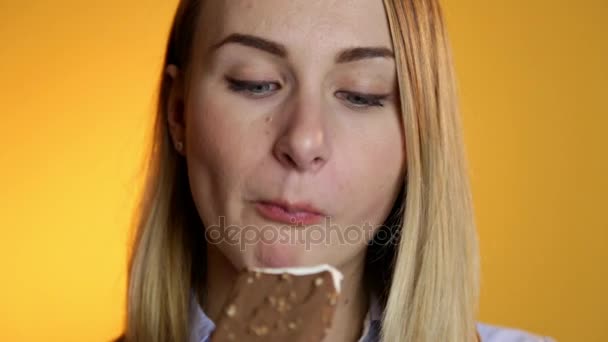 Mujer joven comiendo helado sobre un fondo amarillo — Vídeos de Stock