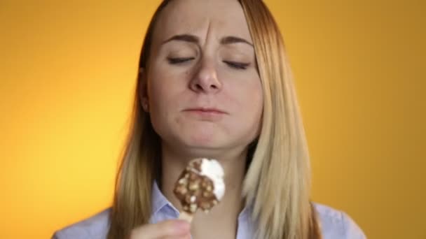 Junge Frau isst Eis auf gelbem Hintergrund — Stockvideo