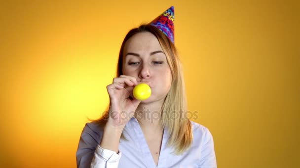 Hermosa chica soplando globos sobre un fondo amarillo — Vídeos de Stock