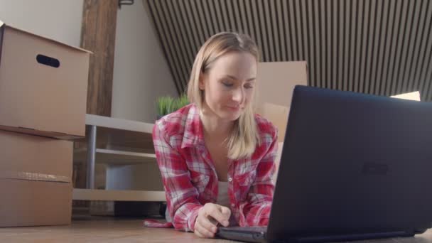Frau sitzt an ausgepackten Kisten mit Laptop — Stockvideo