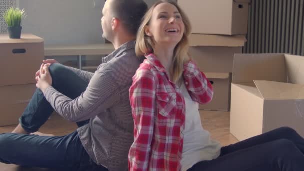 Casal jovem relaxante e rindo depois de desempacotar caixas de movimento de casa — Vídeo de Stock
