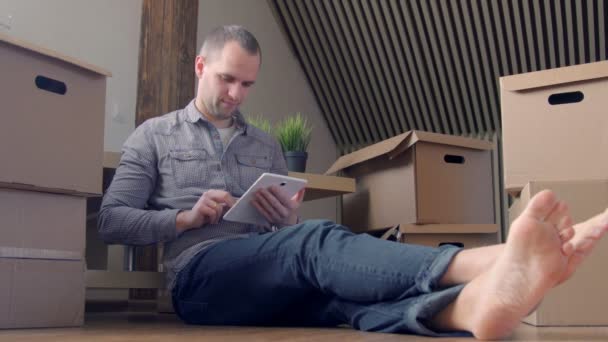 Dolly shot of young smiling man moving to a new house and using digital tablet — Stock Video