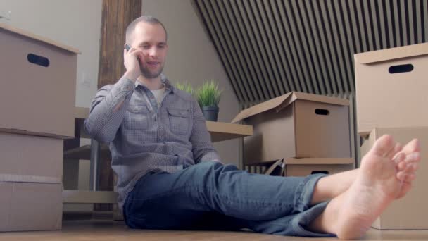 Человек, сидящий возле коробок и разговаривающий по телефону — стоковое видео