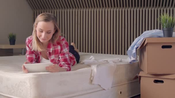 Mujer acostada en el colchón en su nuevo piso y usando en la tableta . — Vídeos de Stock