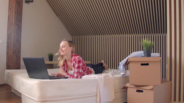 Junge blonde Frau, die morgens auf dem Bett liegt und am Laptop arbeitet, Handschuss. — Stockvideo