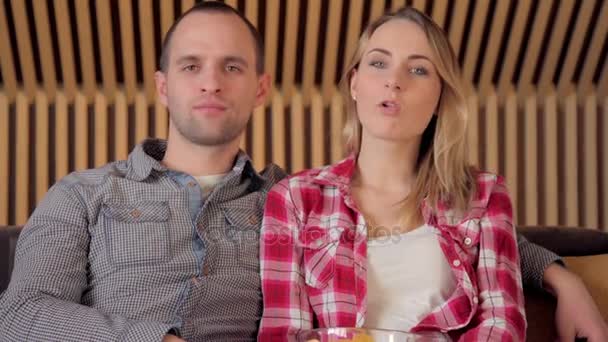 Pareja joven viendo la televisión en el sofá en la sala de estar terminan comiendo patatas fritas — Vídeos de Stock