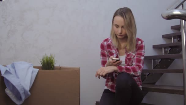 Привлекательная молодая женщина, сидящая на лестнице с помощью мобильного телефона — стоковое видео