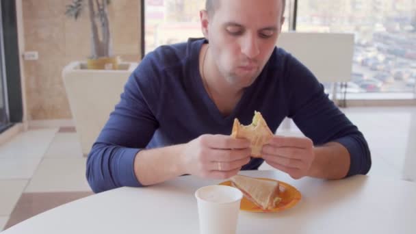 Молодой человек ест сэндвич, завтрак в ресторане — стоковое видео