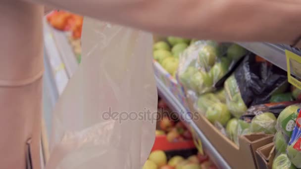 Женщина выбирает свежие красные яблоки в продуктовом отделе и кладет их в пластиковый пакет. Молодая красивая девушка выбирает яблоки в супермаркете и кладет их в корзину — стоковое видео