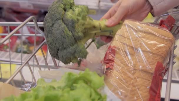 Giovane donna che spinge il carrello lungo i corridoi della spesa nel supermercato. Ragazza che sceglie verdure fresche in drogheria e metterli nel carrello della spesa — Video Stock