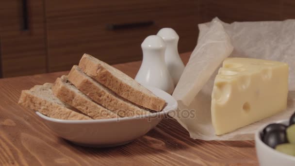 Pan, trozo de queso y aceitunas en cuencos blancos — Vídeo de stock