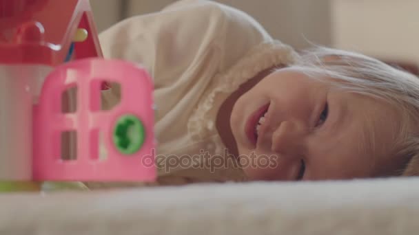 Маленька дівчинка лежить у ліжку і дивиться на камеру . — стокове відео