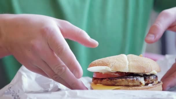 おいしいハンバーガーは、テーブルに最適です。男は彼の手を取るし、食べる、味をみてください。 — ストック動画