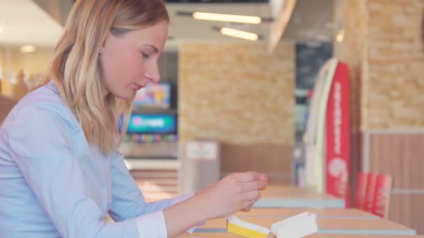 Joven chica bonita está comiendo un donut en la cafetería — Vídeos de Stock