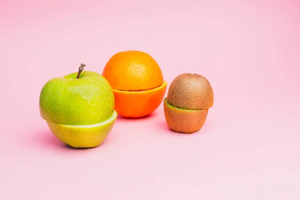 Yarım kesilmiş meyve: bir yeşil elma, portakal ve kivi üzerinde bir pastel pembe arka plan.