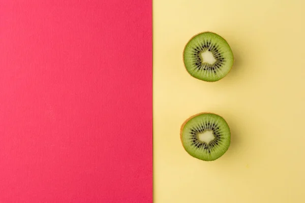 Pastel sarı ve kırmızı zemin üzerine Yarım kesimli kivi. 