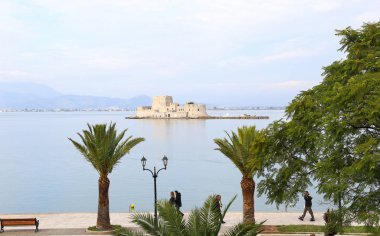 Nafplio Yunanistan, 18 Kasım 2018: Bourtzi Kalesi 'nin önündeki Nafplio limanında yürüyen insanlar. Düzenleyici kullanımı.
