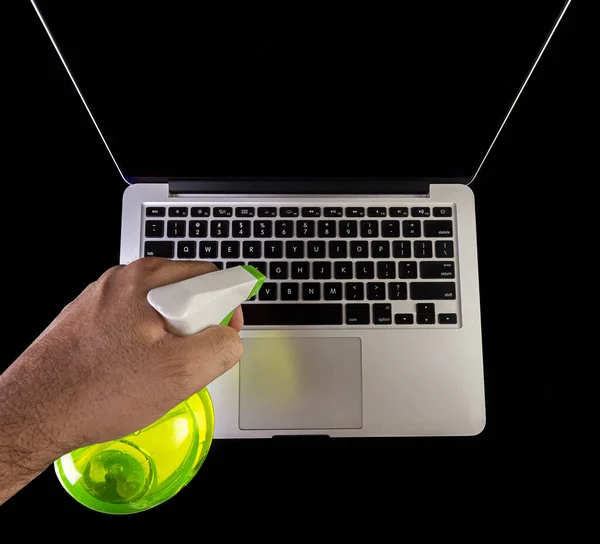 Hand cleaning a laptop with a spray bottle sanitizer