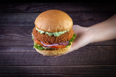 Elleri marul, domates, mor soğan ve ahşap sırtlı el yapımı mayonez ile tavuk burger tutuyor. Lezzetli.