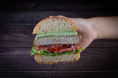 Elleri marul, domates, mor soğan ve ahşap sırtlı el yapımı mayonez ile tavuk burger tutuyor. Lezzetli.