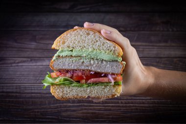 Elleri marul, domates, mor soğan ve ahşap sırtlı el yapımı mayonez ile tavuk burger tutuyor. Lezzetli.