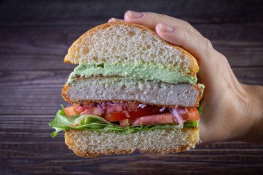 Elleri marul, domates, mor soğan ve ahşap sırtlı el yapımı mayonez ile tavuk burger tutuyor. Lezzetli.