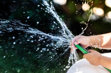 Çocuk bahçede su fıskiyesiyle oynuyor.