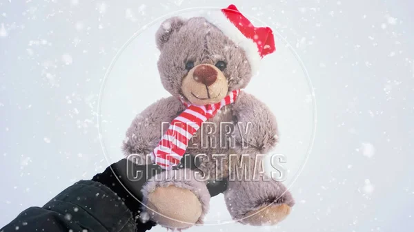 Female hand holding a cute Christmas teddy bear against snow on — Stock Photo, Image