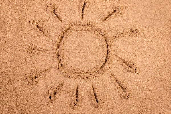 Солнце, нарисованное в мягком влажном песке на пляже
