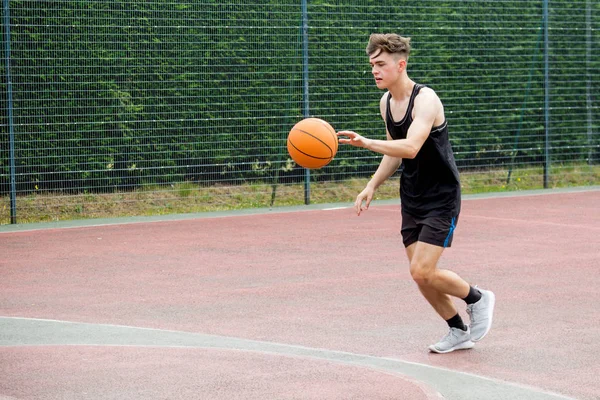 Teenager-Junge, der einen Basketball auf einem Platz hüpft — Stockfoto