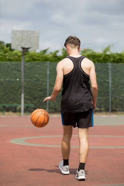 Хлопчик-підліток підстрибує у баскетбол на дворі — стокове фото