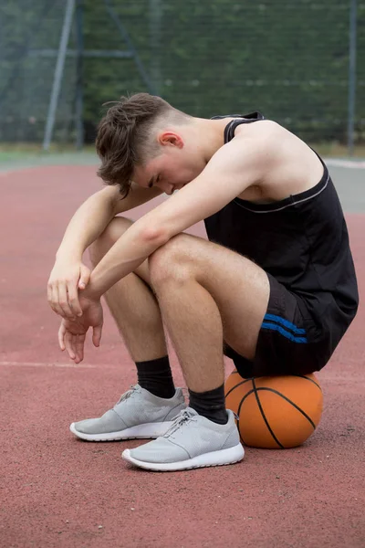 Tizenéves fiú ül a kosárlabda a bíróságon keresnek szomorú — Stock Fotó
