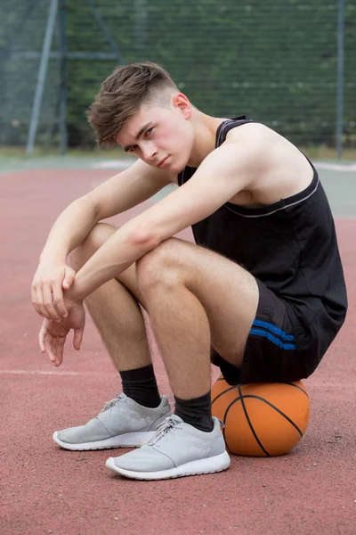 Teenager sitzt auf einem Basketballfeld und sieht traurig aus — Stockfoto