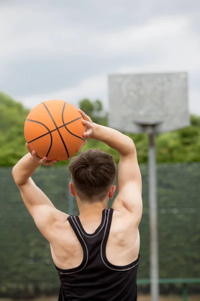 Tonårspojke skytte en hoop på en basketplan — Stockfoto