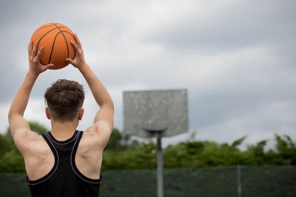 Tonårspojke skytte en hoop på en basketplan — Stockfoto