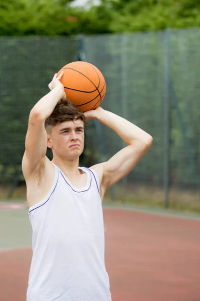 Tonårspojke skytte en hoop på en basketplan — Stockfoto