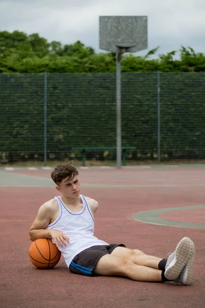 Adolescente sentado em um campo de basquete — Fotografia de Stock
