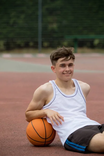 Nastoletni chłopiec siedzi na boisko do koszykówki — Zdjęcie stockowe