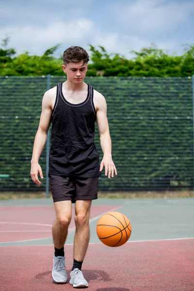 Teenager-Junge, der einen Basketball auf einem Platz hüpft — Stockfoto