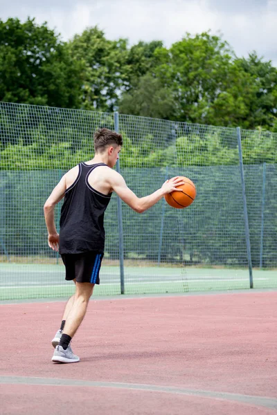 Adolescente saltando uma bola de basquete em um tribunal — Fotografia de Stock