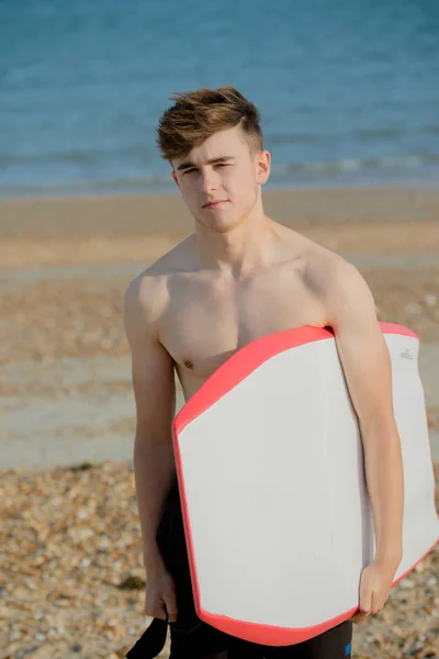 Teenager hält am Strand ein Brett in der Hand — Stockfoto