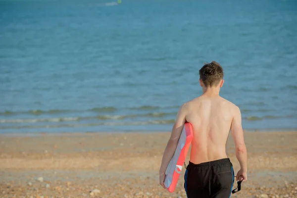 Teenager hält am Strand ein Brett in der Hand — Stockfoto