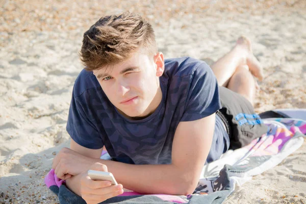 Nastoletni chłopak na plaży przy użyciu telefonu komórkowego — Zdjęcie stockowe