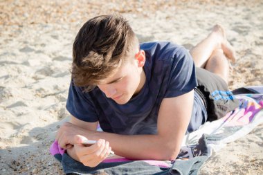 Genç çocuk bir cep telefonu kullanarak bir kumsalda döşeme