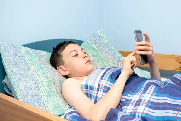 Jovem caucasiano adolescente usando seu telefone na cama — Fotografia de Stock