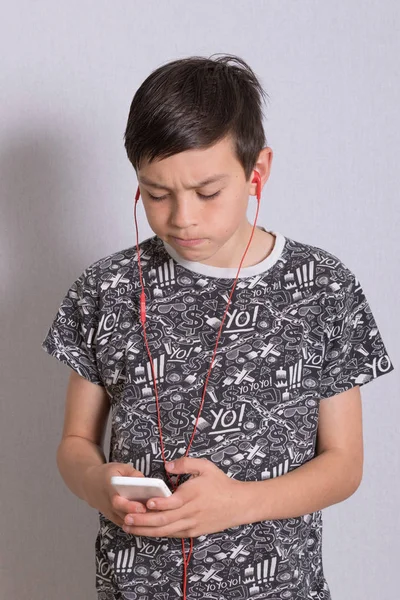 Niño escuchando música desde su teléfono con auriculares — Foto de Stock